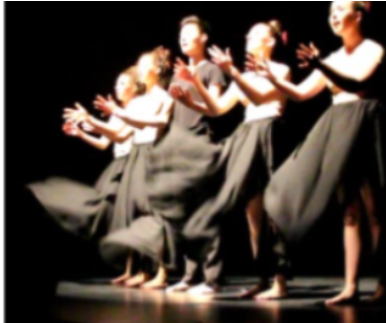 Students in long black skirts extend their arms gracefully on a stage