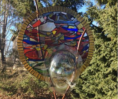 glass mural in circular shape with colourful depictions inside of boats, glass face hangs on top
