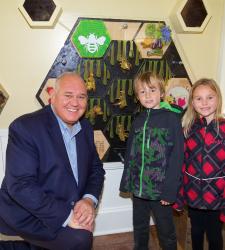 An adult and two kids smiling at the camera in front of an interactive honeycomb.
