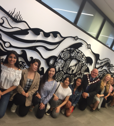 A group of people kneeling in front of the Aaniin Community Centre mural